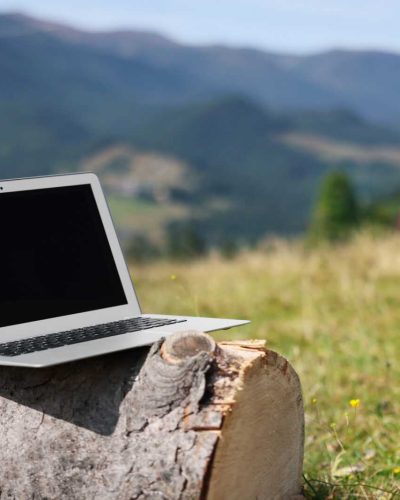 Laptop on wooden log in mountains, space for text. Distance work